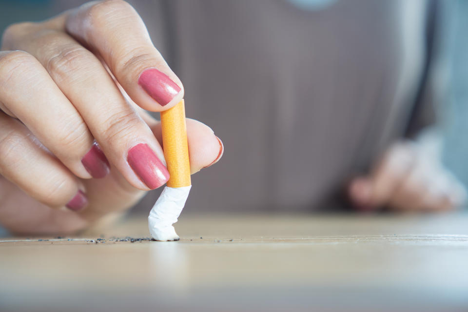 A hand with painted fingernails extinguishes a cigarette on a table