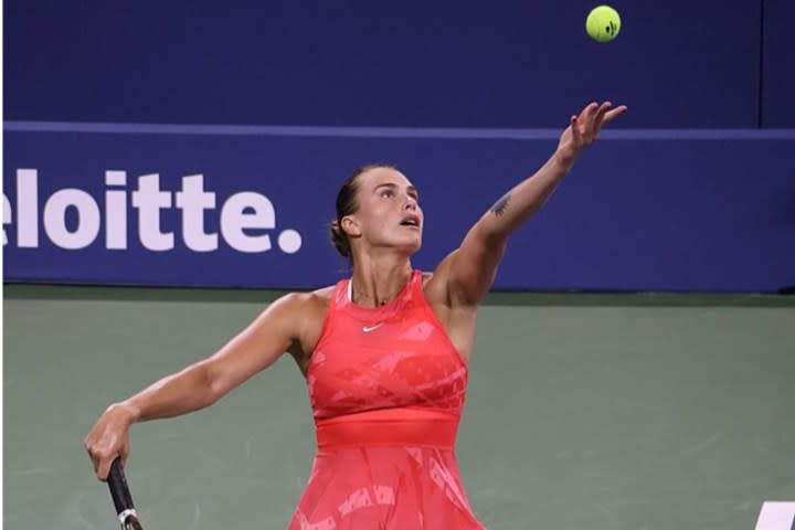 A female tennis player throws a tennis ball in the air.