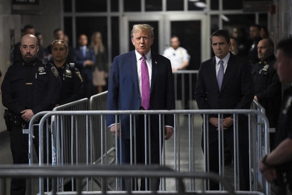 Donald Trump speaks with the media from behind barriers in a Manhattan criminal courthouse hallway.