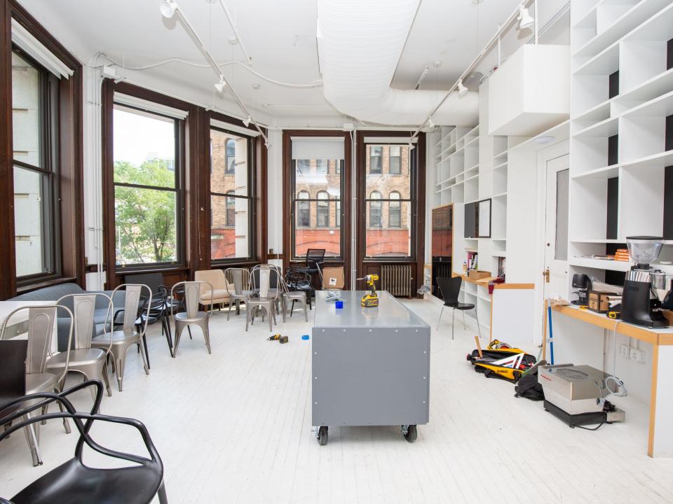 A room full of large windows, shelves, chairs, a workstation.