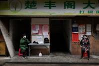 Volunteers wearing face masks keep watch at an entrance to a residential building in Wuhan