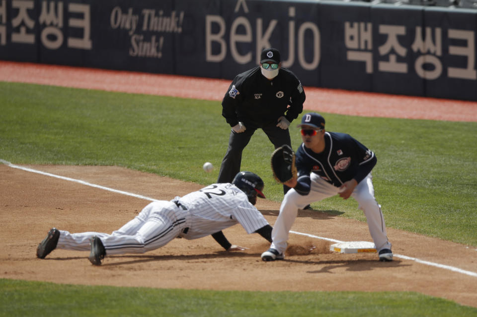 First base umpire Lee Gye-sung, center, wearing a mask and gloves as a precaution against the new coronavirus looks on during the pre-season baseball game between Doosan Bears and LG Twins in Seoul, South Korea, Tuesday, April 21, 2020. South Korea's professional baseball league has decided to begin its new season on May 5, initially without fans, following a postponement over the coronavirus. (AP Photo/Lee Jin-man)