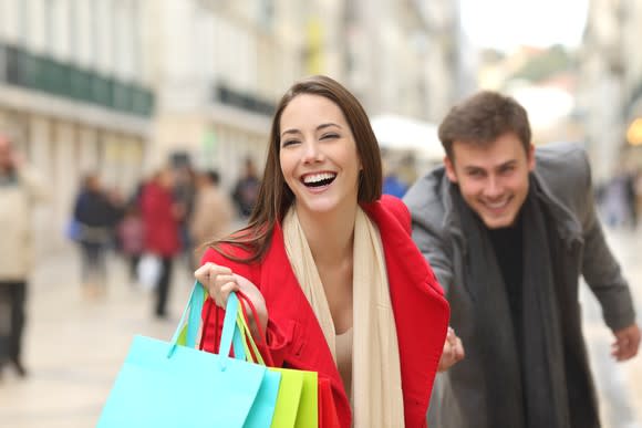 A happy young couple races across a city street, carrying shopping bags.