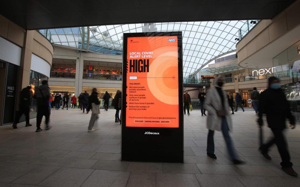 Shoppers walk past a NHS sign displaying the Local Covid Alert Level as 'high' in the centre of Leeds -  LINDSEY PARNABY / AFP