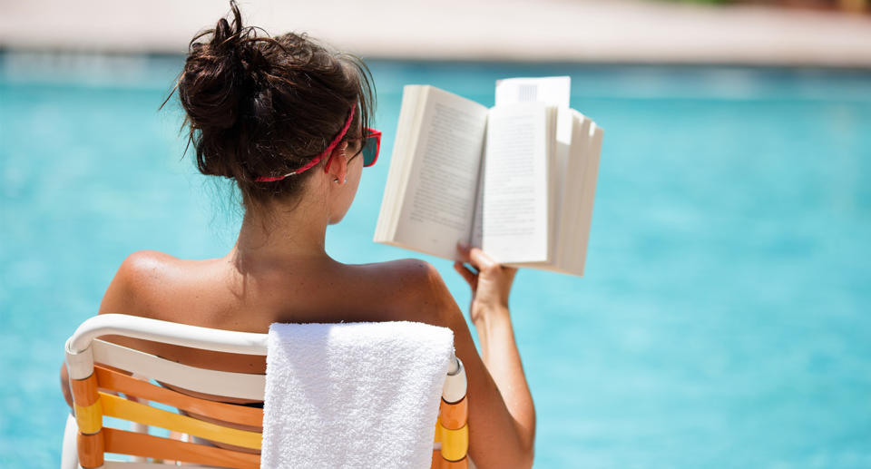  Woman on annual leave sitting by the pool reading on holiday. (Getty Images)