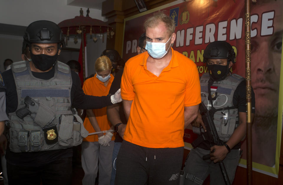 Indonesian police officers escorted Andrei Kovalenka, center, and his partner Ekaterina Trubkina, walks behind during a news conference at immigration office in Jimbaran, Bali, Indonesia on Wednesday, Feb. 24, 2021. Kovalenka, a Russian listed by the Interpol as a fugitive back home was arrested on the Indonesian tourist island of Bali on Wednesday after 13 days on the run with his partner to avoid deportation. (AP Photo/Firdia Lisnawati)