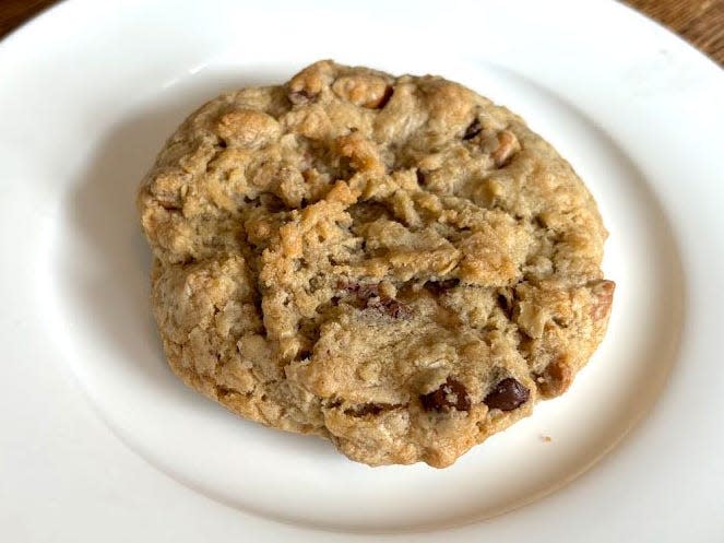 An oatmeal chocolate-chip Crumbl cookie with peanut butter and toffee chips on a white plate. The plate is on a wooden table.