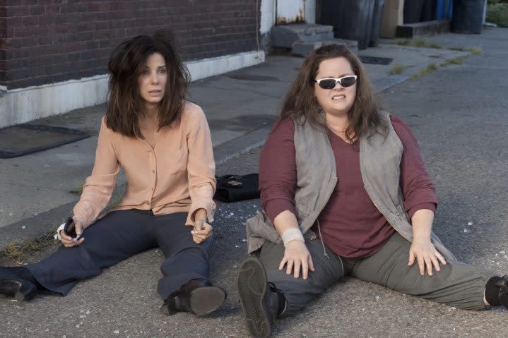 Two women sit down next to each other on the ground.