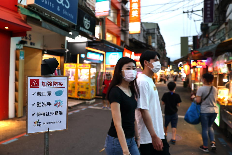 People wearing protective face masks walk past a sign reading 