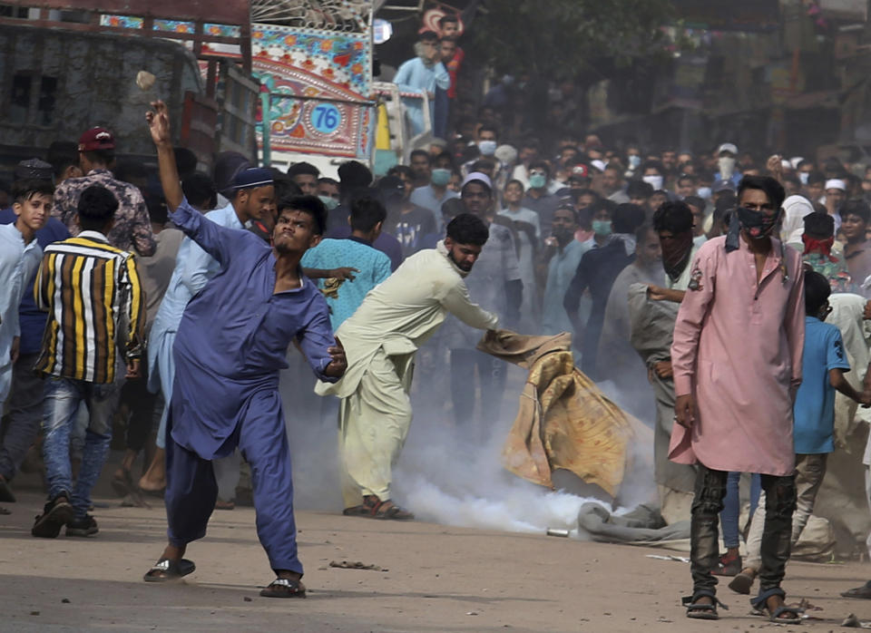 A supporter of Tehreek-e-Labiak Pakistan, a banned Islamist party, throws a stone while another tries to extinguish a tear gas canister fired by police to disperse protests over the arrest of their party leader Saad Rizvi, in Karachi, Pakistan, Monday, April 19, 2021. The outlawed Islamist political group freed 11 policemen almost a day after taking them hostage in the eastern city of Lahore amid violent clashes with security forces, the country's interior minister said Monday. (AP Photo/Fareed Khan)