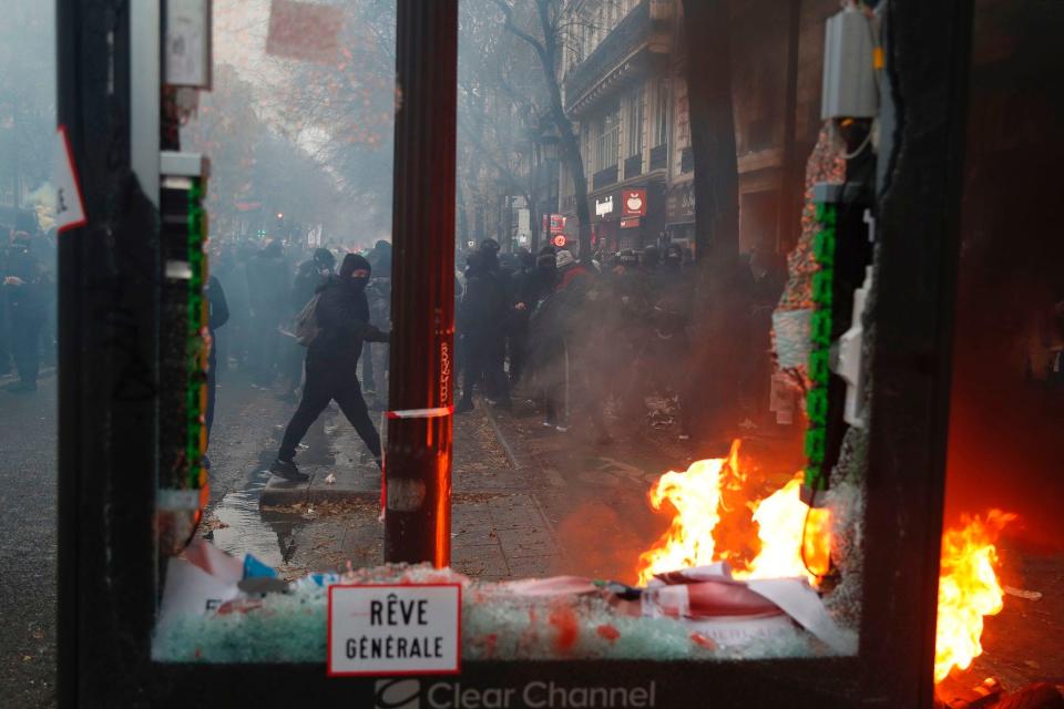   Protesters are seen through a broken electronic billboard next to a burning item during a rally against the pension overhauls, in Paris, on December 5, 2019 as part of a nationwide strike.  