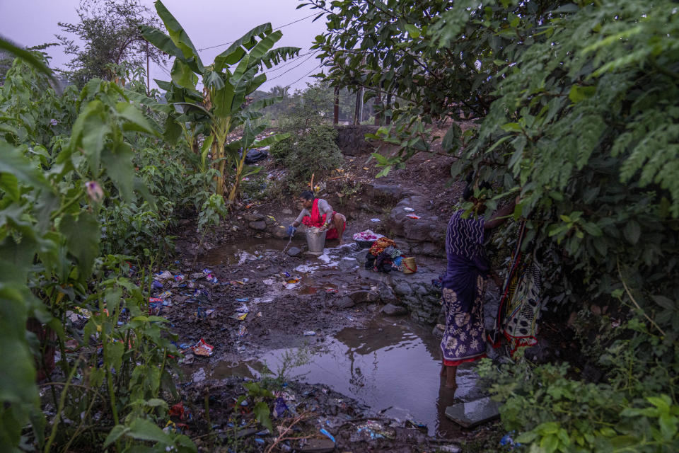 Rekha Wagh, right, washes clothes as another woman collects water for washing early in the morning by a sewer near Shahapur, northeast of Mumbai, India, Saturday, May 6, 2023. She said, "I have been getting up before sunrise to wash clothes since my childhood. Even here, there are a lot of quarrels later in the day to find a spot." (AP Photo/Dar Yasin)