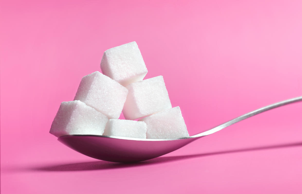 Close up of a spoon pilled high with sugar cubes on pink background