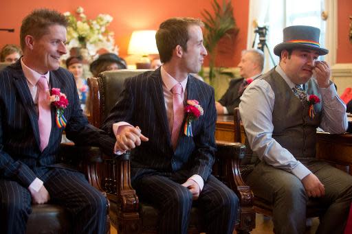 Phil Robathan (i) y James Preston (c) se dan la mano cuando un invitado a su boda reacciona emocionado durante la ceremonia en Brighton, en el sur del Inglaterra, el 29 de marzo de 2014 (AFP | Leon Neal)