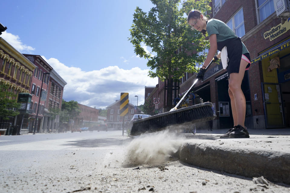 Deli worker Annabelle Morland sweeps dried mud from the sidewalk weeks after flood waters destroyed downtown, Tuesday, Aug. 1, 2023, in Montpelier, Vt. The mostly gutted shops, restaurants and businesses that lend downtown Montpelier its charm are considering where and how to rebuild in an era when extreme weather is occurring more often. Vermont's flooding was just one of several major flood events around the globe this summer that scientists have said are becoming more likely due to climate change. (AP Photo/Charles Krupa)