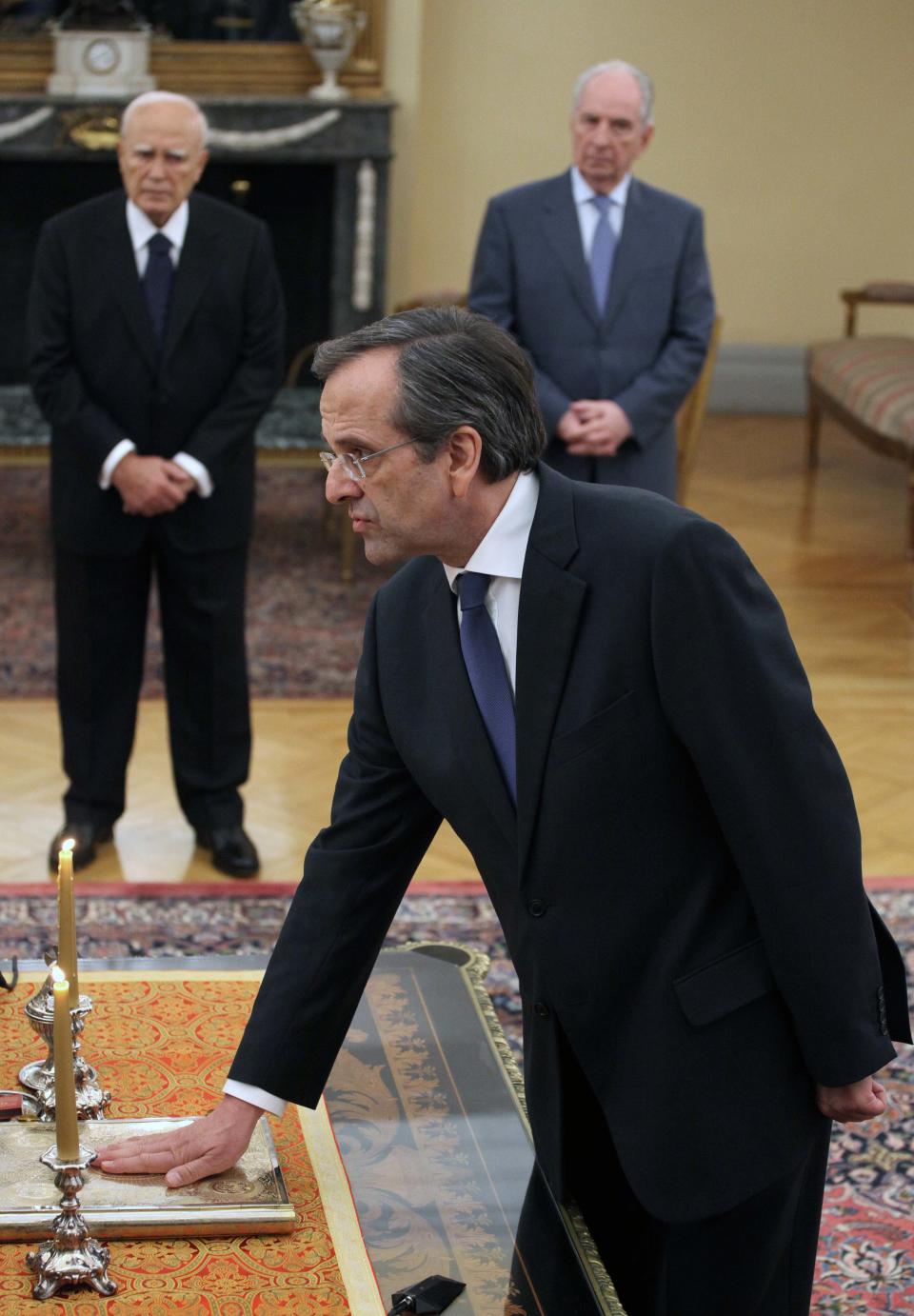 Greek conservative New Democracy leader Antonis Samaras is sworn in during a ceremony at the Presidential Palace as Greek president Karolos Papoulias, background left, looks on, in Athens, on Wednesday, June 20, 2012. Samaras was sworn in as prime minister Wednesday at the helm of a three-party coalition that will uphold the country’s international bailout commitments. The move ends a protracted political crisis that had cast grave doubt over the country’s future in Europe’s joint currency and threatened to plunge Europe deeper into a financial crisis with global repercussions. (AP Photo/Petros Giannakouris)