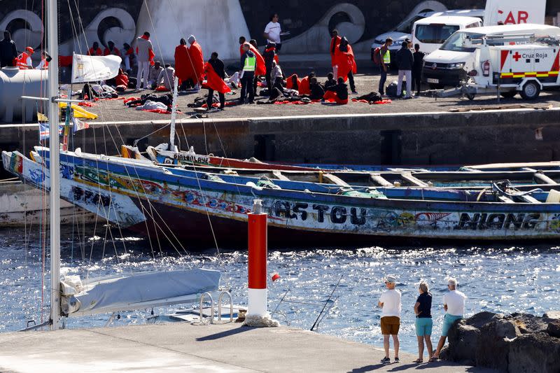 Several tourists observe migrants getting treated as they arrive, at the port of La Restinga