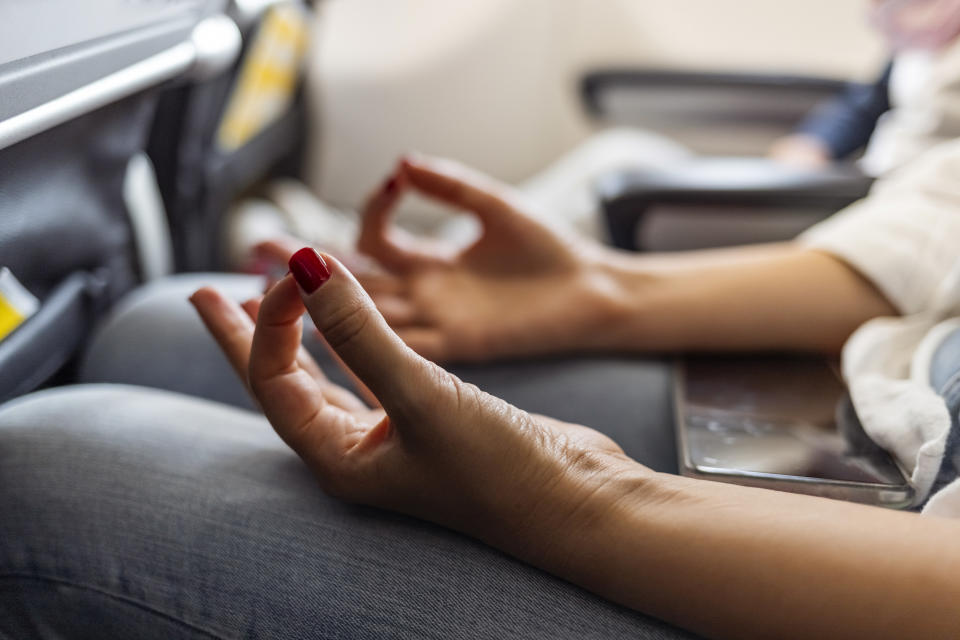 Female Person in airplane with aerophobia scared of flying being afraid while sitting in airplane seat and doing yoga for relax