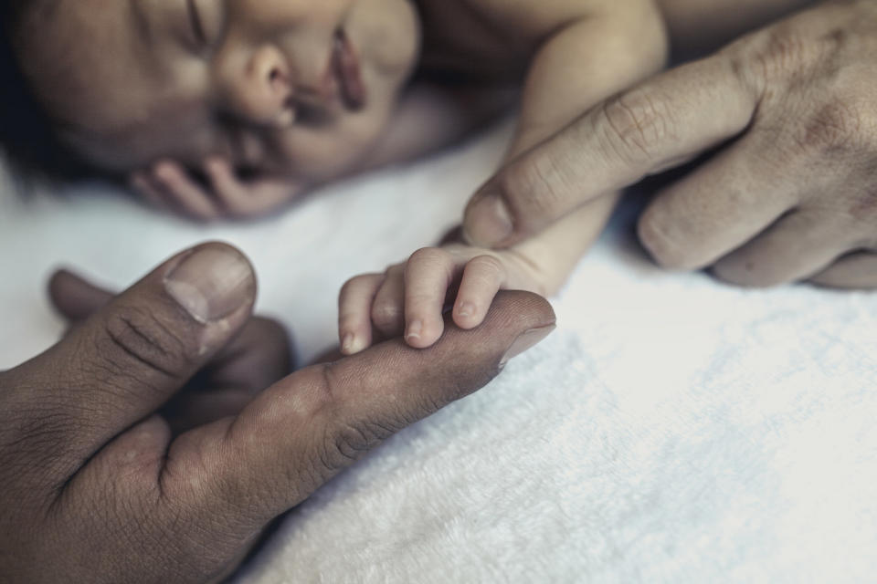 A newborn born through IVF holds his father's finger with his tiny hand