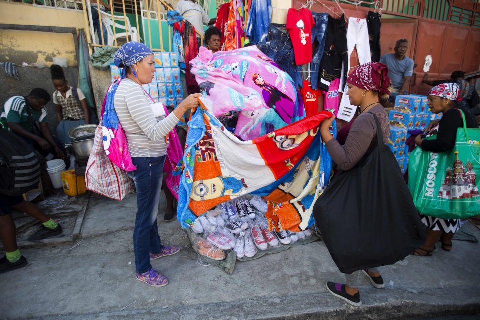 Cuban shoppers hold up a bed cover as they shop at a street market in Port-au-Prince, Haiti, Thursday, Dec. 6, 2018. Since Cuba did away with a hated exit permit five years, Cubans are packing flights to destinations with easy entry requirements: Port-au-Prince, Panama City, Cancun, Guyana, Trinidad and Tobago, even Moscow, where they are packing suitcases with goods for personal use and resale back home. (AP Photo/Dieu Nalio Chery)