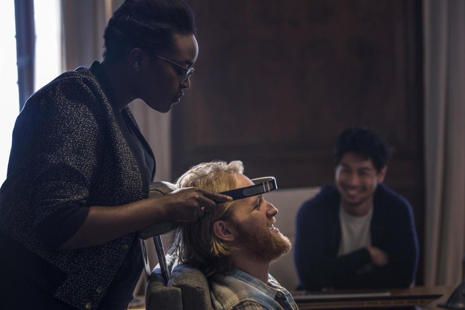 A woman puts an experimental device atop the head of a bearded video game tester