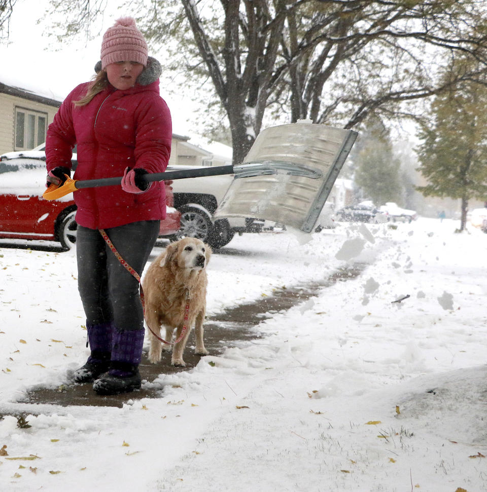 Gianni Green shovels snow off her neighbor's sidewalk along Avenue K in Scottsbluff, Neb., before going to school Thursday, Oct. 10, 2019. Green's golden retriever Sadie accompanied her as she cleared the sidewalk. (Lauren Brant/The Star-Herald via AP)