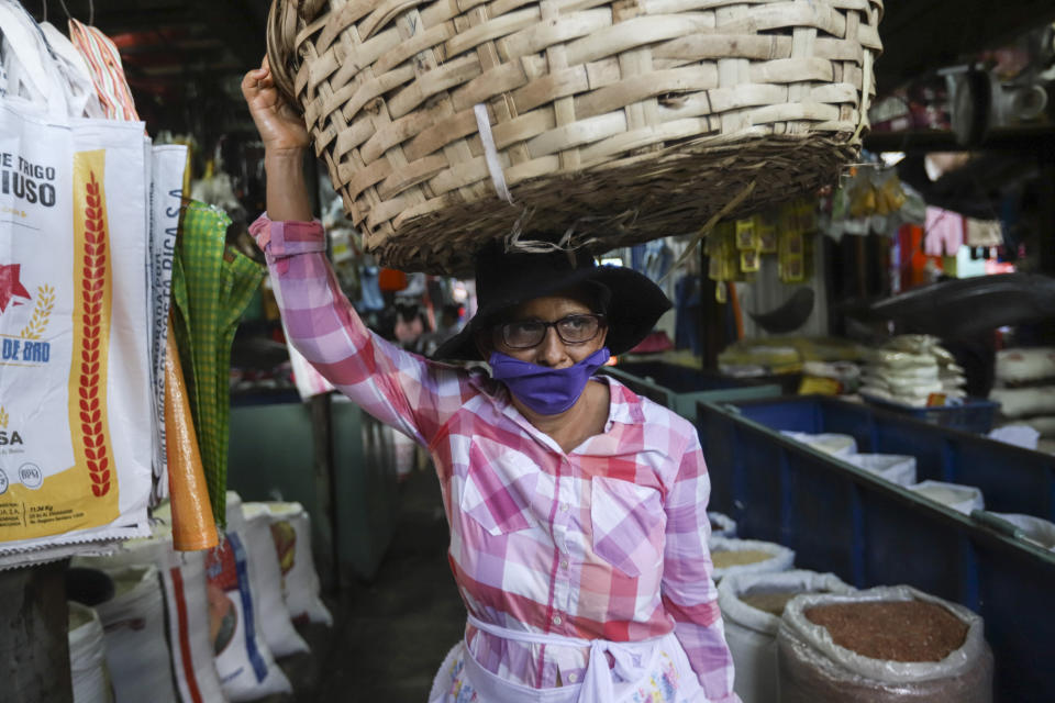 A fruit vendor, wearing a protective face mask, makes her way through a popular market in Managua, Nicaragua, Tuesday, April 7, 2020. Restaurants are empty, there's little traffic in the streets and beach tourists are sparse headed into Holy Week despite the government's encouragement for Nicaraguans to go about their normal lives. (AP Photo/Alfredo Zuniga)