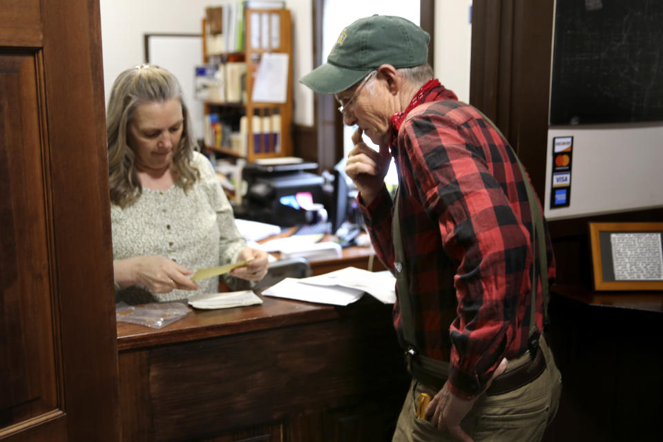 Victory Town Clerk Tracey Martel, left, helps town resident Will Staats buy dog licenses in Victory, Vt., Thursday, March 31, 2022. Martel says she's regularly frustrated watching a spinning circle on her computer while she tries to complete even the most basic municipal chores online. It could be years before high-speed internet reaches Victory. The need to connect homes and businesses to high-speed broadband services was highlighted by the COVID-19 pandemic and officials say that while there is lots of money available, supply and labor shortages are making the expansion a challenge. (AP Photo/Wilson Ring)