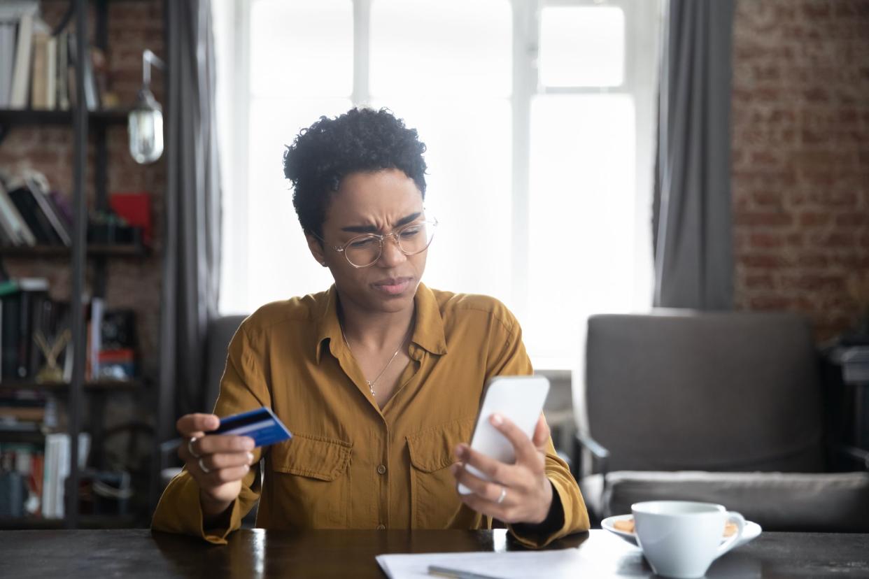 Unhappy nervous young African American woman in glasses looking at smartphone screen, feeling stressed entering wrong payment information from bank credit card, having problems with internet shopping.