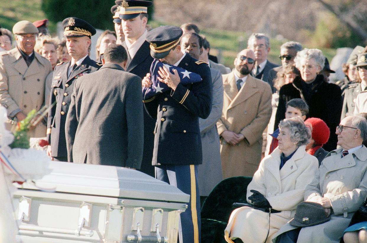 Major Marie T. Rossi of Oradell, N.J., receives a full Honor funeral at Arlington National Cemetery on Monday, March 11, 1991. Undersecretary of the Army John W. Shannon presents the flag to Rossi's husband, Chief Warrant Officer Three John R. Cayton, as her parents Paul and Gertrude Rossi seated to the right look on. Rossi was killed in a helicopter crash on March 1, 1991, in Saudi Arabia. (AP Photo/Dennis Cook)