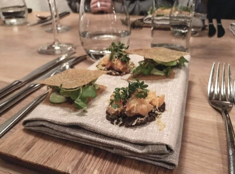 Hors d'oeuvres of some kind with crackers and garnish, served on a folded napkin on top of a wood cutting board