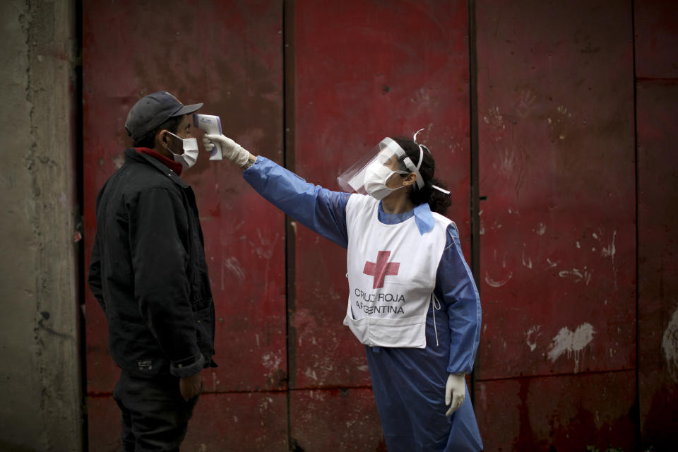 Una voluntaria de la Cruz Roja mide la temperatura de un residente dentro del barrio marginal de Fraga durante un confinamiento ordenado por el gobierno para frenar la propagación del nuevo coronavirus, en Buenos Aires, Argentina, el sábado 6 de junio de 2020. (Foto AP/Natacha Pisarenko)