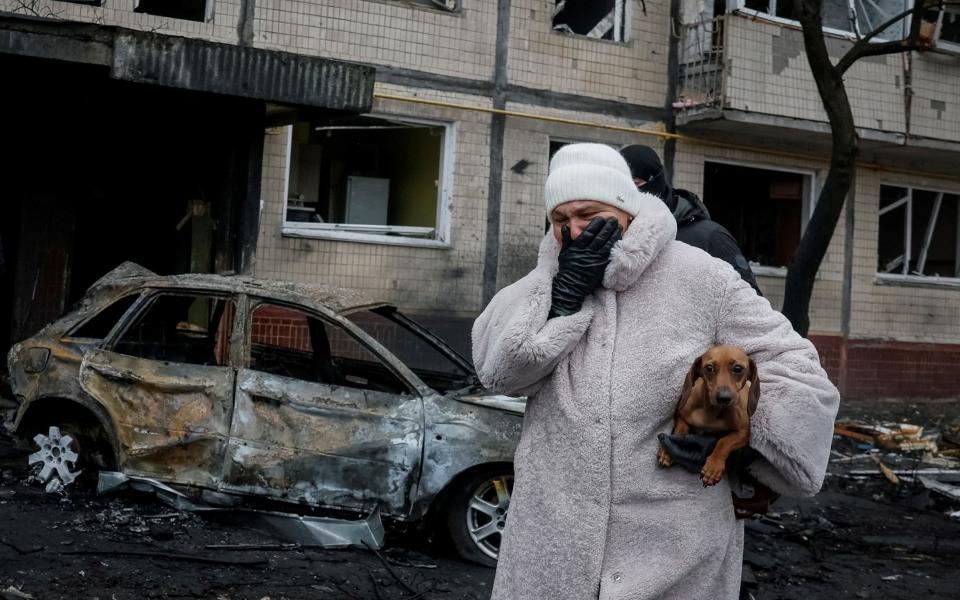 A local covers his mouth in shock as she walks in front of a burned out car