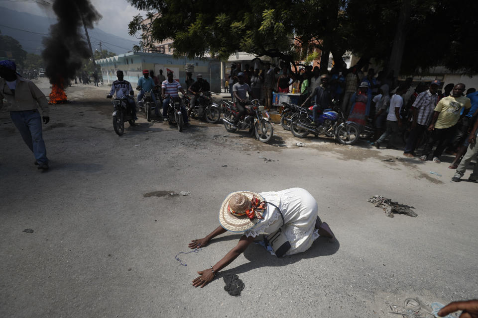 A churchgoer drops to the ground and prays in the street near burning tires lit by protesters, during a march called by religious leaders in Port-au-Prince, Haiti, on Oct. 22, 2019. (AP Photo/Rebecca Blackwell)