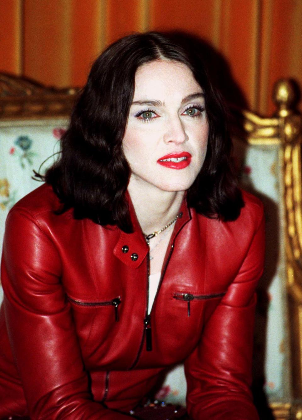 Madonna smiles during a news conference in Stockholm November 14, wearing a red leather jacket with zips, with black shoulder-length hair worn loose.  