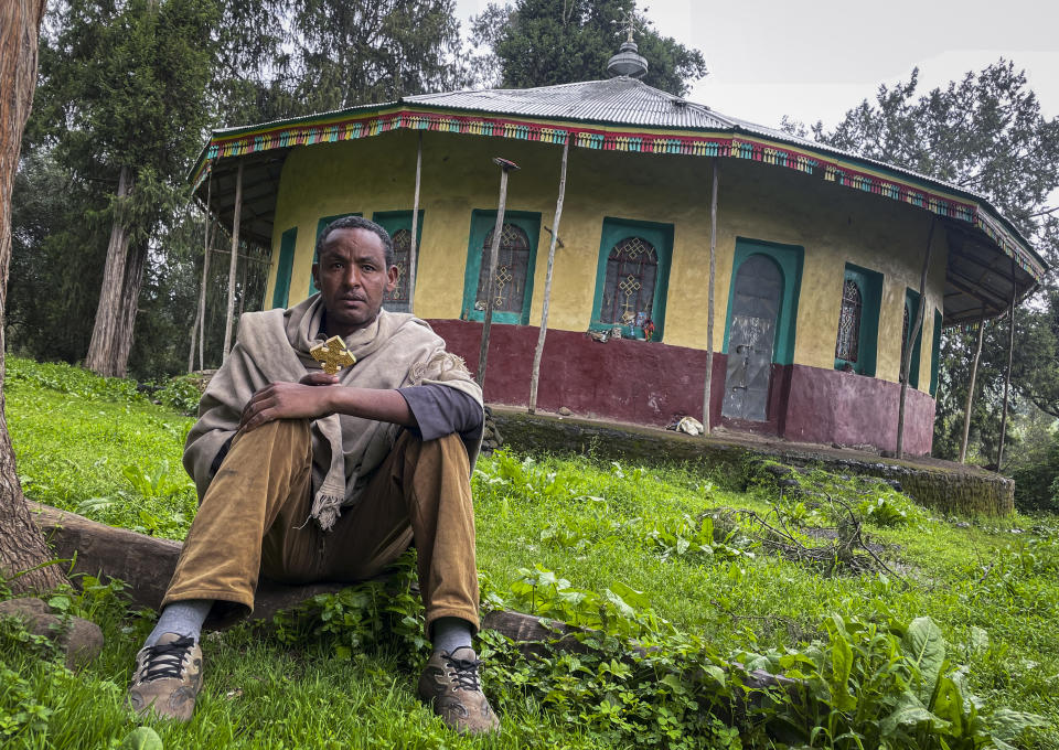 Priest Yared Adamu holds an Ethiopian Orthodox cross in the churchyard where residents say more than 50 civilians have been laid to rest in makeshift graves, in the village of Chenna Teklehaymanot in the Amhara region of northern Ethiopia Thursday, Sept. 9, 2021. At the scene of one of the deadliest battles of Ethiopia's 10-month Tigray conflict, witness accounts reflected the blurring line between combatant and civilian after the federal government urged all capable citizens to stop Tigray forces "once and for all." (AP Photo)