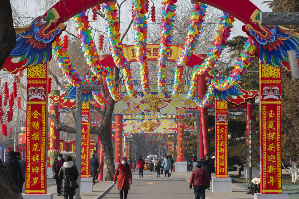 People wearing face masks walk under a canopy decorated with spinning colored fans for a canceled Lunar New Year temple fair at Longtan Park in Beijing, Saturday, Jan. 25, 2020. China's most festive holiday began in the shadow of a worrying new virus Saturday as the death toll surpassed 40, an unprecedented lockdown kept 36 million people from traveling and authorities canceled a host of Lunar New Year events. (AP Photo/Mark Schiefelbein)