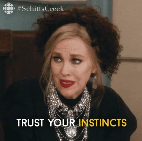 Catherine O'Hara as Moira Rose from Schitt's Creek, wearing an elaborate necklace and dramatic makeup, with the caption "Trust your instincts."