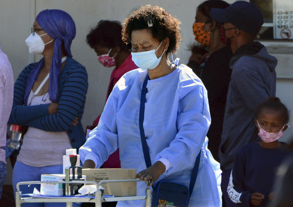 A healthcare worker pushes her trolley past people queuing to be tested for COVID-19 at the Livingstone Hospital in Port Elizabeth, South Africa, Friday, Nov. 13, 2020. The Eastern Cape Province is seeing a surge in cases of coronavirus and has recorded the highest number of COVID-19-related deaths in the country. (AP Photo/Theo Jeptha)