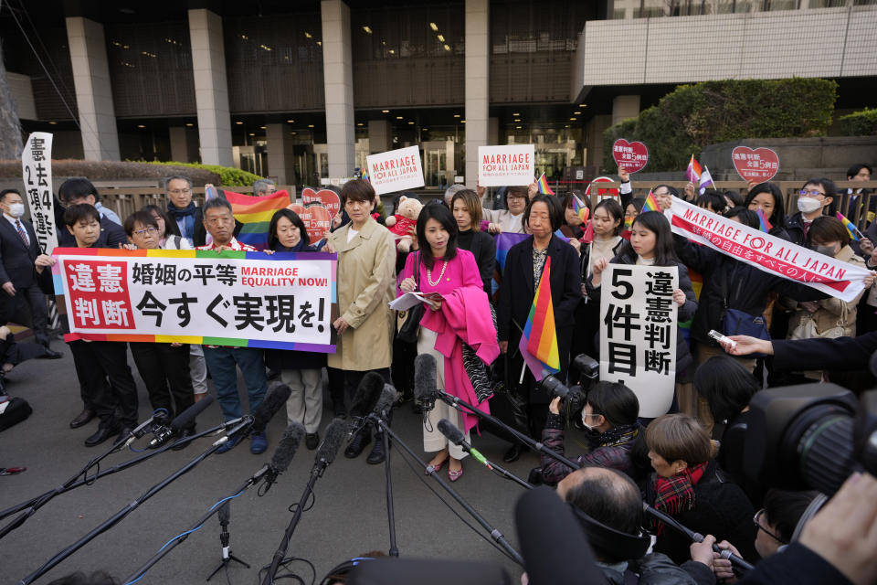 A lawyer, in pink clothes, center, for the plaintiffs standing to her right speaks in front of media members by the main entrance of the Tokyo district court after hearing the ruling regarding LGBTQ+ marriage rights, in Tokyo, Thursday, March 14, 2024. The Japanese court on Thursday ruled that not allowing same-sex couples the same marital benefits as heterosexuals violates their fundamental right to have a family, but the current civil law did not take into consideration sexual diversity and is not clearly unconstitutional, a partial victory for Japan's LGBTQ+ community calling for equal marriage rights. (AP Photo/Hiro Komae)