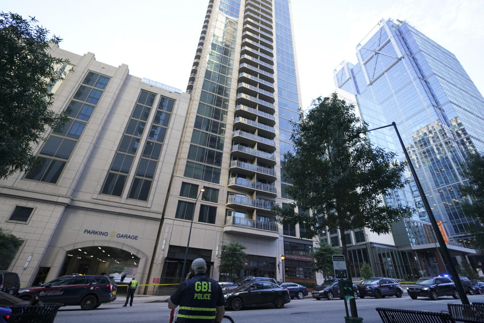 A police officer stands near the entrance of a residential building, Wednesday, Oct. 20, 2021, in Atlanta. Police in Atlanta have closed streets around at least four square blocks of office and apartment buildings in response to gunfire in the city's midtown area. (AP Photo/Brynn Anderson)