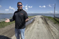 In this May 10, 2019 photo, Brett Adams gestures as he stands where the road to his flooded farm disappears under flood waters, with the farm buildings seen in the background, in Peru, Neb. Adams had thousands of acres under water, about 80 percent of his land, this year. The water split open his grain bins and submerged his parents' house and other buildings when the levee protecting the farm broke. (AP Photo/Nati Harnik)