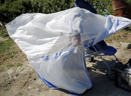 A boy covers himself with a net during heavy winds at a makeshift camp for migrants and refugees at the Greek-Macedonian border near the village of Idomeni, Greece, April 20, 2016. REUTERS/Stoyan Nenov