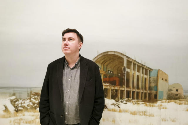 In this photo taken on Sunday, Feb. 17, 2019, Pavel Otdelnov, a Russian artist poses for a photo in front of his work "Ruins #4" at his an exhibition in Moscow, Russia . Pavel Otdelnov, a Russian artist who grew up in Dzerzhinsk, the center of the nation's chemical industries 355 kilometers (220 miles) east of Moscow, focused on the city, one of the most polluted in Russia, in his new 'Promzona' art show. (AP Photo/Ivan Kochkarev)