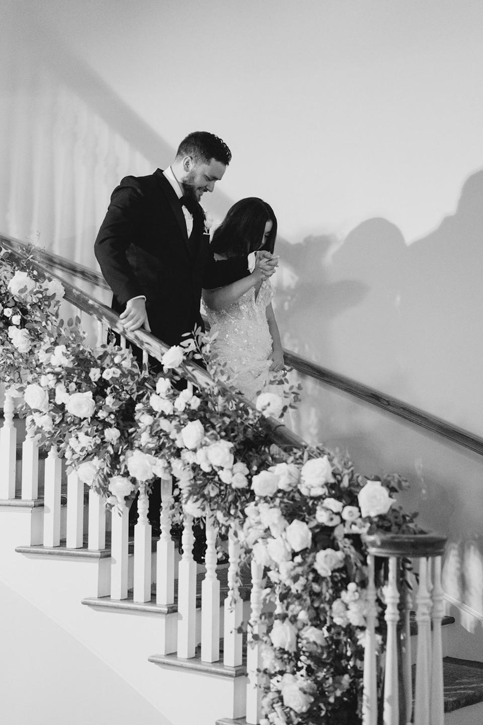 A bride and groom walk down stairs covered in flowers together.