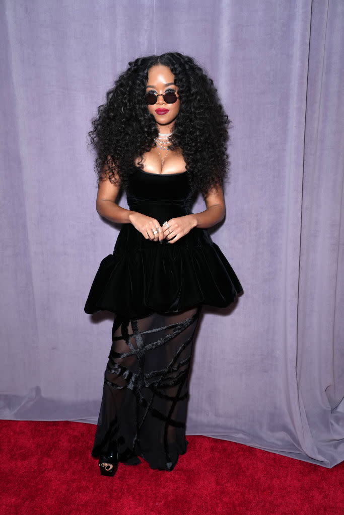 H.E.R. in black, low-cut gown with black bustle skirt.