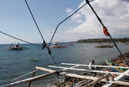 A fisherman repairs his boat overlooking fishing boats that fish in the disputed Scarborough Shoal in the South China Sea, at Masinloc, Zambales, in the Philippines April 22, 2015. REUTERS/Erik De Castro