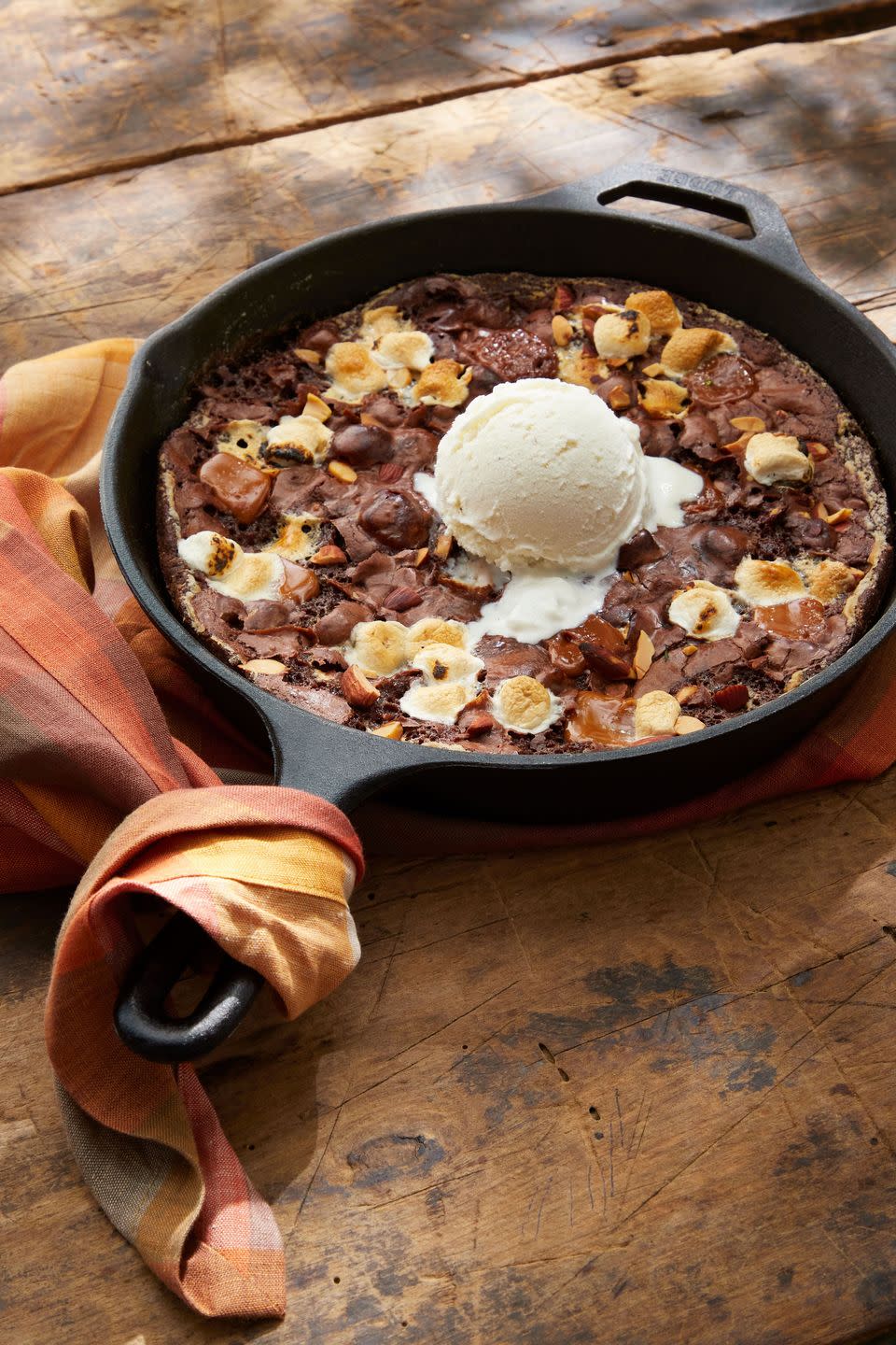 brownies baked in a cast iron skillet with caramel marshmallows and salted almonds with a scoop of vanilla ice cream on top