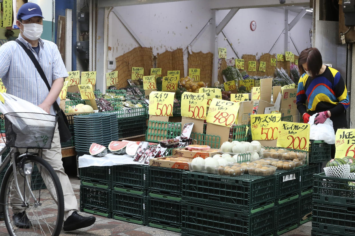 A man wearing a face mask to protect against the spread of the new coronavirus walks a bicycle past a shop selling fruits and vegetables in Yokohama near Tokyo, Wednesday, May 13, 2020. Japan is still under a coronavirus state of emergency, which was extended this week until the end of May, though there have been no hard lockdowns. (AP Photo/Koji Sasahara)