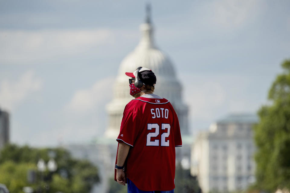 The Dome of the U.S. Capitol is visible as a Washington Nationals fan wearing a Juan Soto jersey walks outside Nationals Park before the New York Yankees and the Washington Nationals play an opening day baseball game, Thursday, July 23, 2020, in Washington. (AP Photo/Andrew Harnik)